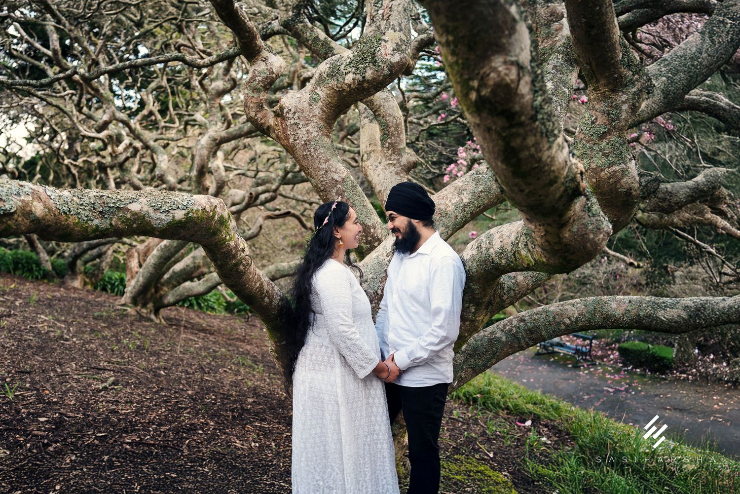 A couple shares a moment beneath the twisted branches of a massive tree.