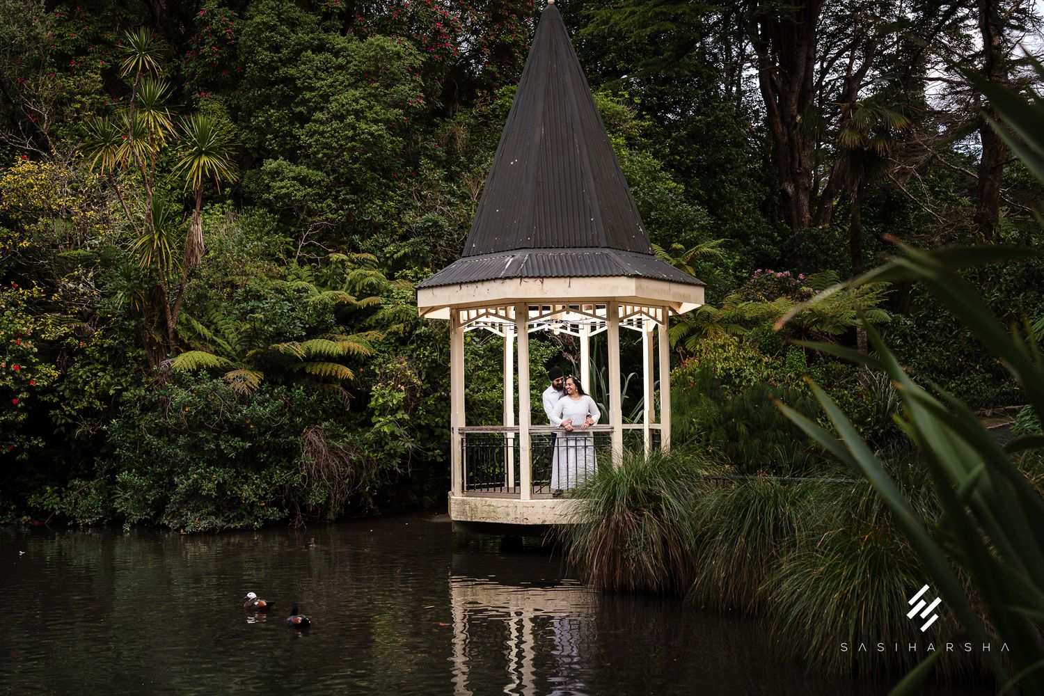 A white gazebo sits peacefully on a lake surrounded by lush greenery and trees.