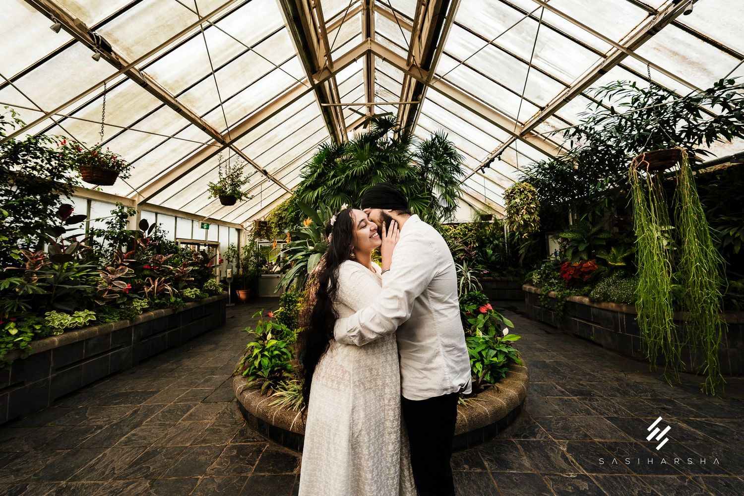 Wide angle view inside a greenhouse conservatory with rows of tropical plants and glass ceiling.