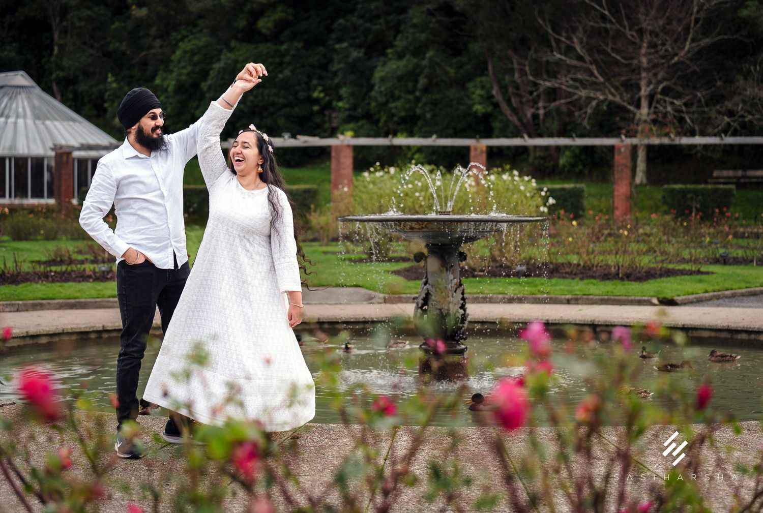 A couple shares an intimate moment in a garden with pink flowers in the foreground.