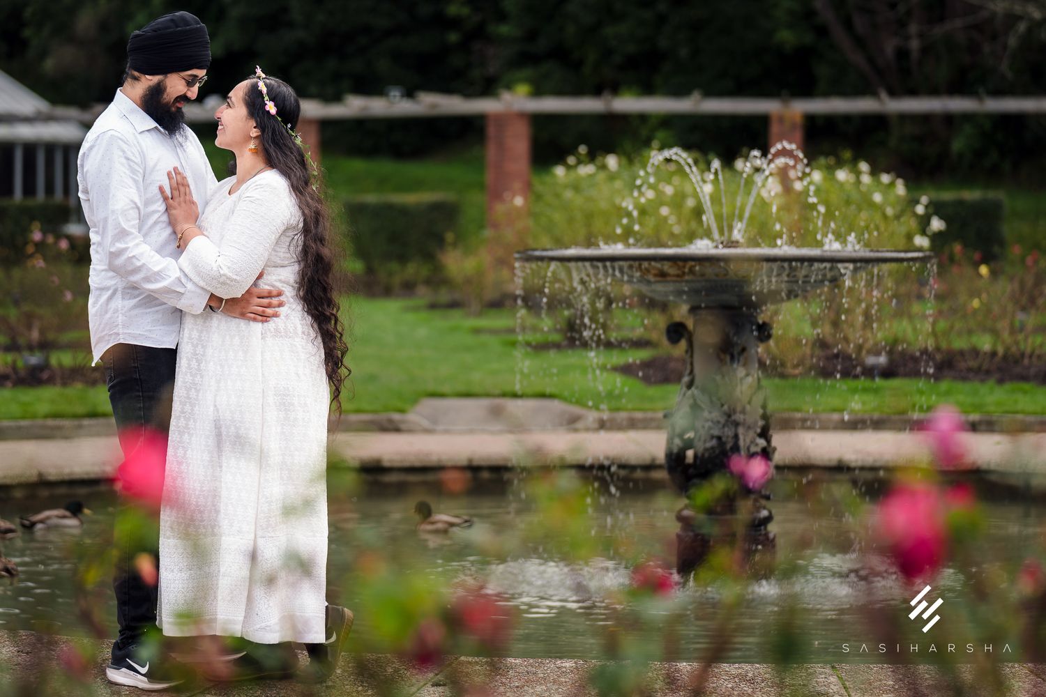 A romantic garden photoshoot with blooming pink flowers and a pond in the background.