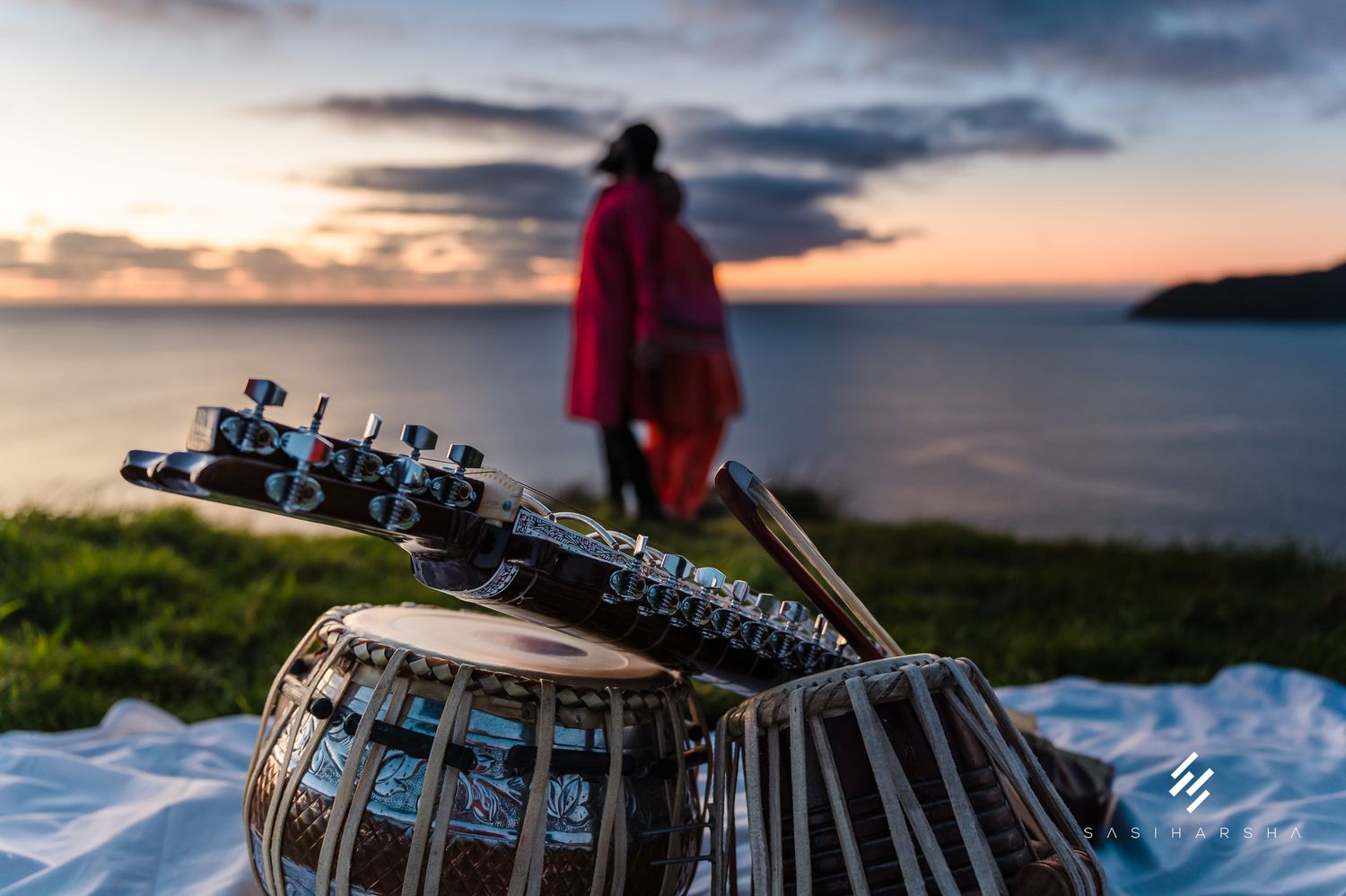 Traditional tabla drums in foreground with a coastal sunset and silhouetted figure in background.