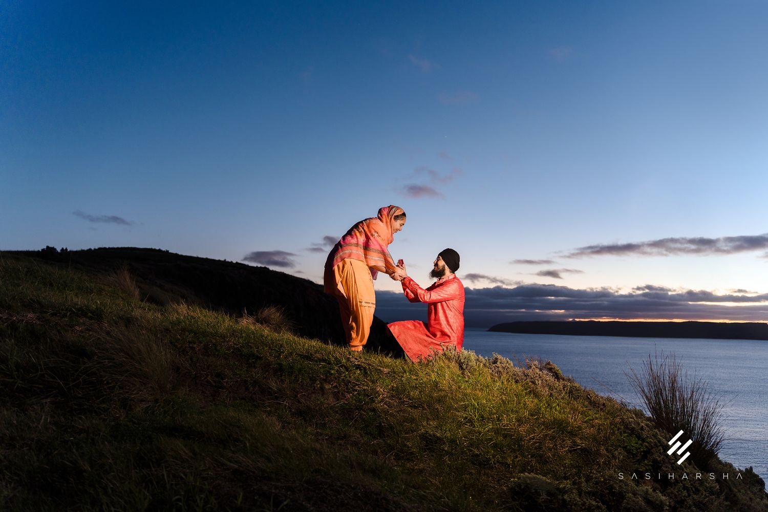 A sunset proposal moment on a coastal hillside overlooking the ocean.