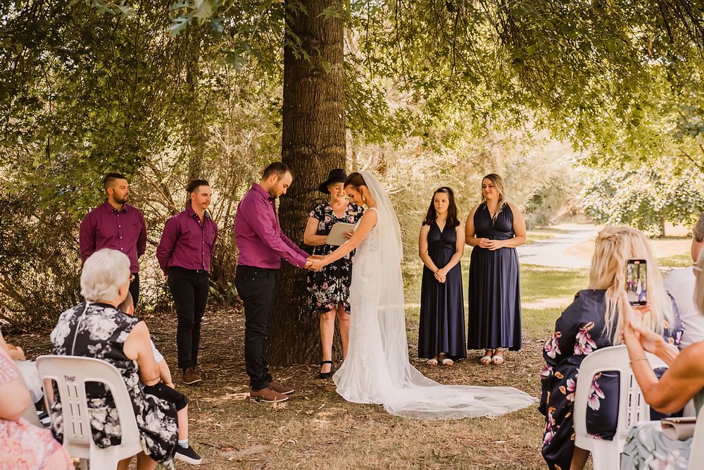 Wedding party celebrating in a garden setting with shady trees and greenery decorations.