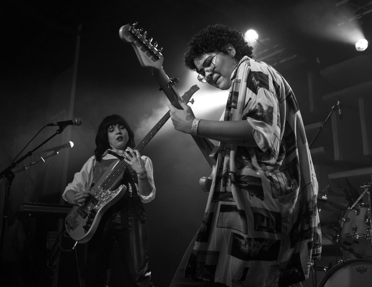Black and white photo of live music performance featuring a guitarist and vocalist on stage. High contrast lighting with expressive motion.