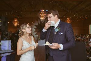 A wedding couple shares cake at their reception under warm indoor lighting.