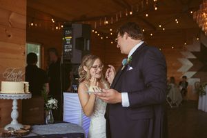 Wedding reception couple cutting cake in rustic barn venue with string lights overhead.