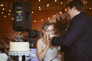 Newlyweds share a playful moment while feeding each other wedding cake under twinkling lights.