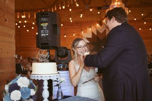 A playful cake-feeding moment between newlyweds at their rustic wedding reception.