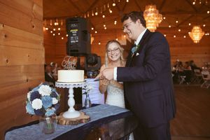Festive barn wedding reception with cake cutting moment under string lights.