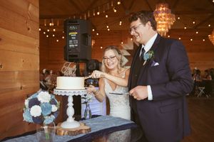 Wedding party celebrates cake cutting moment in rustic barn venue.