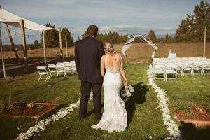 Outdoor wedding ceremony setup with white chairs arranged on a grassy field against a scenic mountain backdrop.