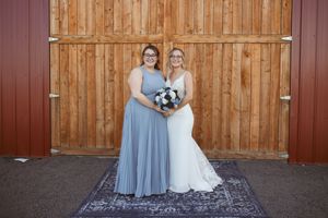 Wedding party poses against wooden barn wall wearing blue bridesmaid dresses.
