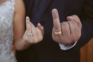 Close-up shot of hands showing wedding rings against a dark background.
