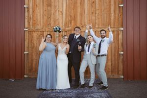 Wedding group photo session in front of rustic red barn with bridal party.
