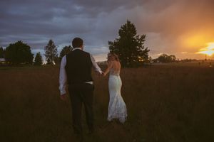 A couple walking together in a field at sunset with dramatic clouds and golden light in the background.
