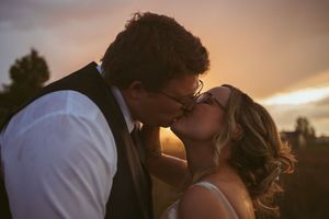 A romantic silhouette of two people sharing a kiss at sunset with warm glowing sky in the background.