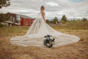 A stunning bridal portrait showcasing a long flowing veil and bouquet against a rustic farmhouse backdrop.