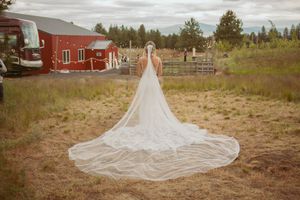 Long flowing wedding dress train trails across rustic outdoor venue grounds.