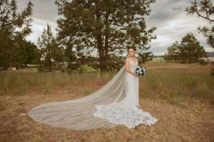 Long cathedral veil and elegant white wedding gown photographed from behind in a natural meadow setting.