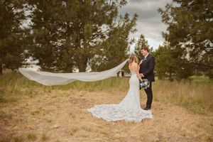A wedding couple embraces in a scenic outdoor setting as the bride's veil flows dramatically in the wind.