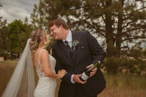 A couple shares a romantic moment outdoors with pine trees and cloudy skies in the background.