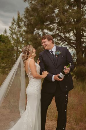 A couple celebrates with champagne against a backdrop of pine trees during their outdoor wedding photoshoot.