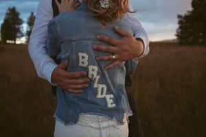 Someone wearing a light blue denim vest with 'BRIDE' text standing in a grassy field at sunset.