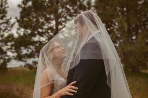 A romantic veil shot captures a tender moment between newlyweds in a natural outdoor setting.
