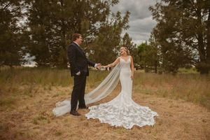Wedding couple dances together on hillside with bride's stunning lace dress train flowing across dry grass.