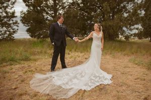 A couple in wedding attire holding hands on a rustic path with a dramatic flowing train on the wedding dress.