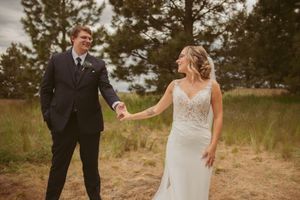 Couple shares playful moment in outdoor wedding photos with bride's lace gown spread beautifully on autumn field.