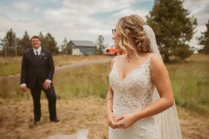 Wedding couple poses in a scenic field with mountain views and cloudy skies.