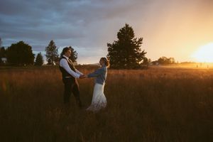 A couple dances in a golden meadow at sunset with tall pine trees silhouetted in the background.