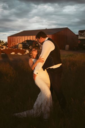 A romantic sunset moment between newlyweds dancing near a rustic red barn under moody clouds.