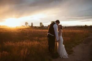 Golden sunset silhouettes a couple in formalwear walking through a rural field.
