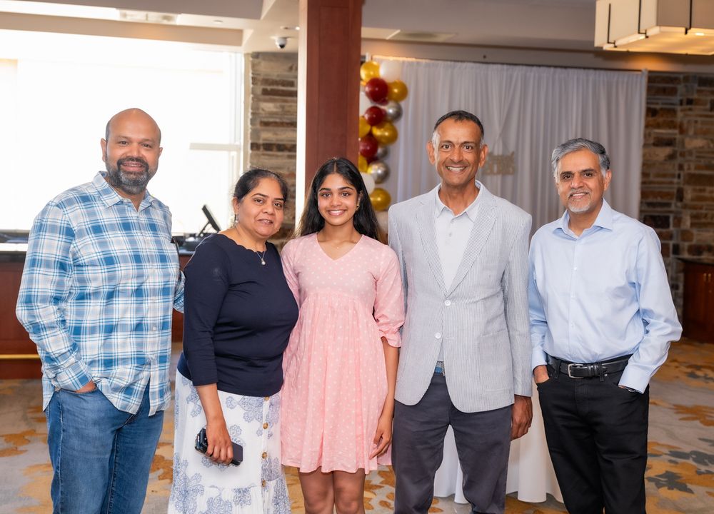 A group of people standing together in various casual outfits in what appears to be a home interior setting.