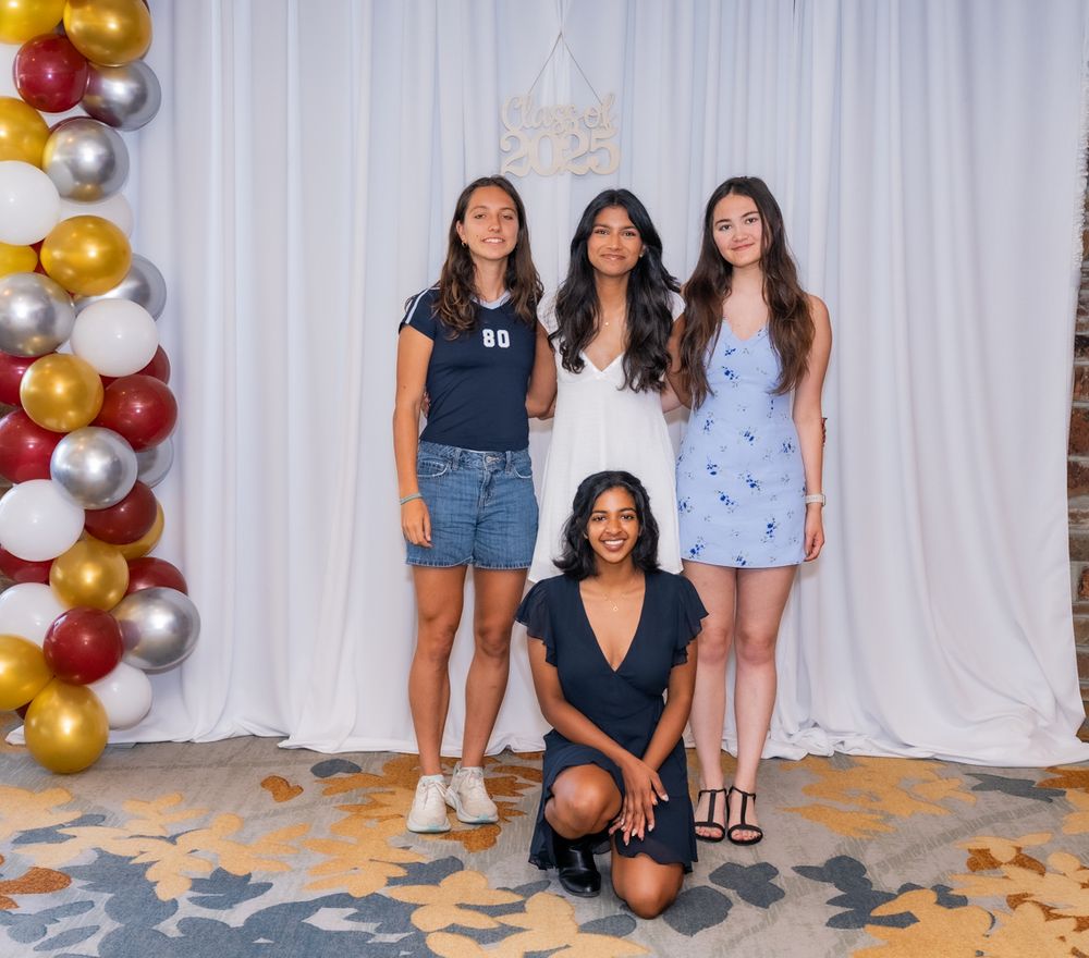 A group of people posing together in front of a white backdrop with gold and silver balloon decorations.