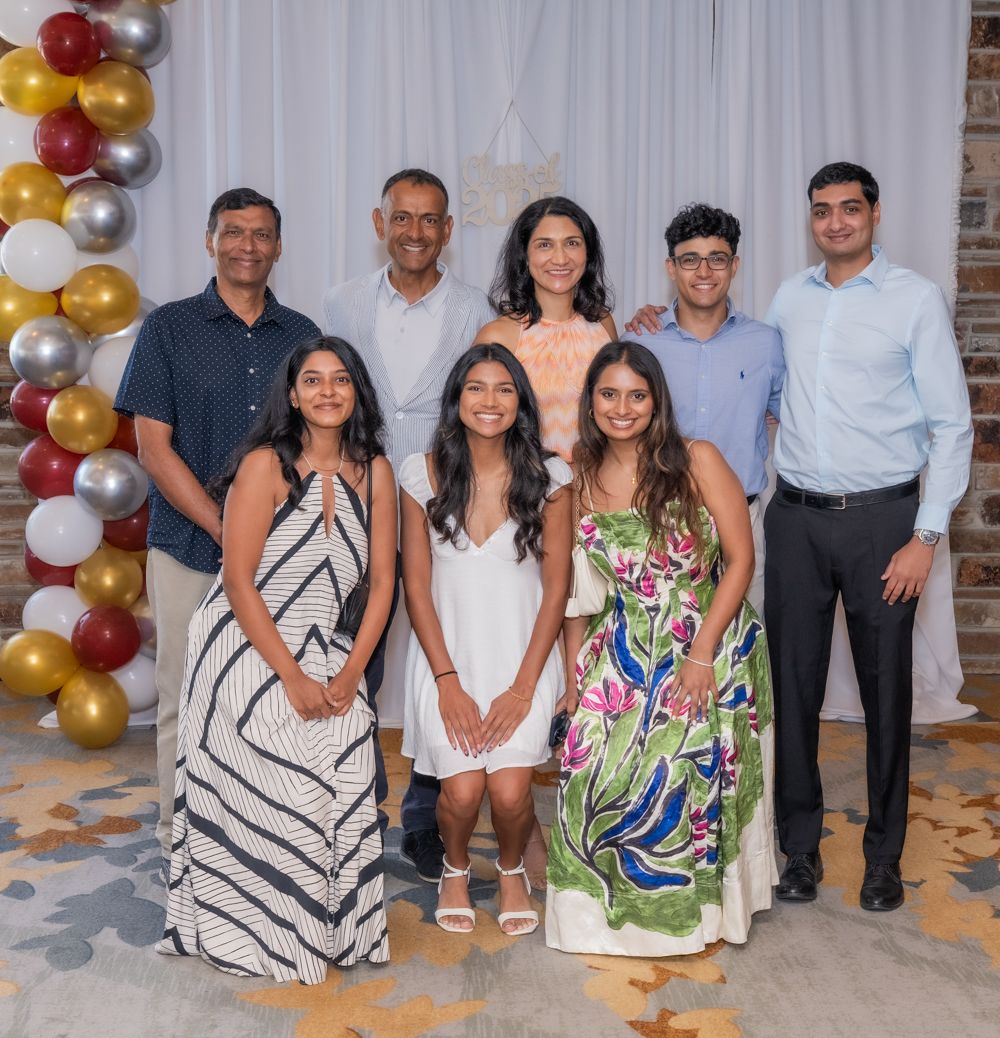 People gathered for a group photo at a special event with gold and silver balloon decorations and white backdrop.