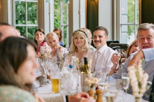 Wedding guests enjoying drinks and conversation during an elegant indoor reception with natural lighting through windows.