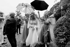 A bride in a white gown and wedding party members hold umbrellas while walking on a rainy wedding day.