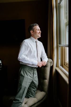 Person in white shirt and grey pants sits near window in moody lighting creating dramatic shadows and atmosphere.