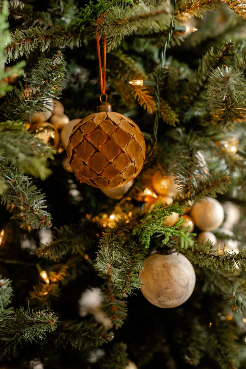 Close-up of gold and white ornaments hanging on a Christmas tree with warm glowing lights.