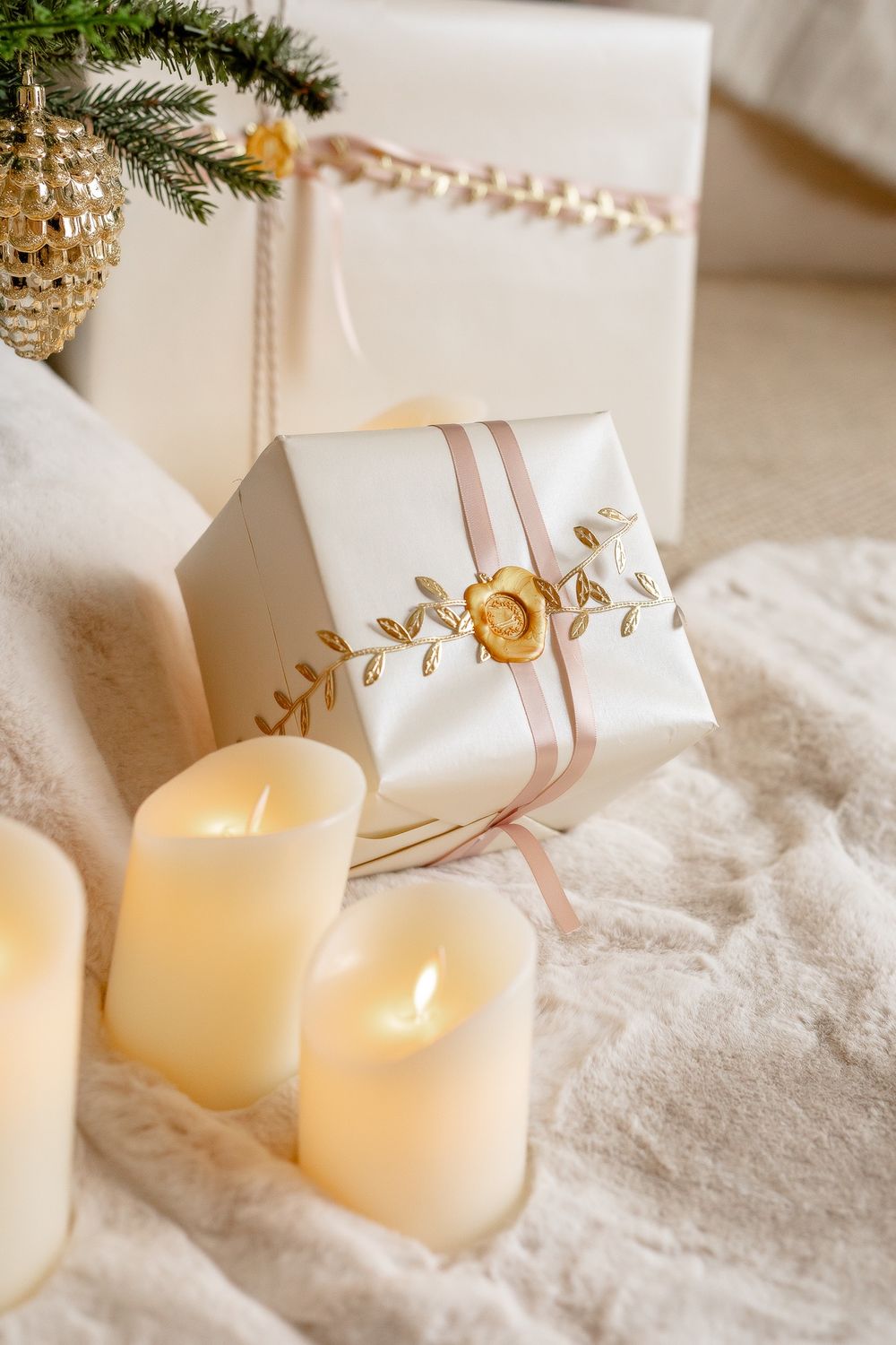 White wrapped Christmas presents nestled in artificial snow beside glowing ivory candles and pine branches.