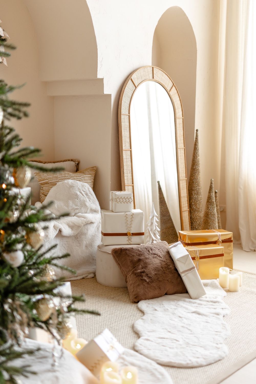 A cozy boho-style holiday scene with an arched mirror, white textiles, pampas grass and Christmas tree decorations in warm light.