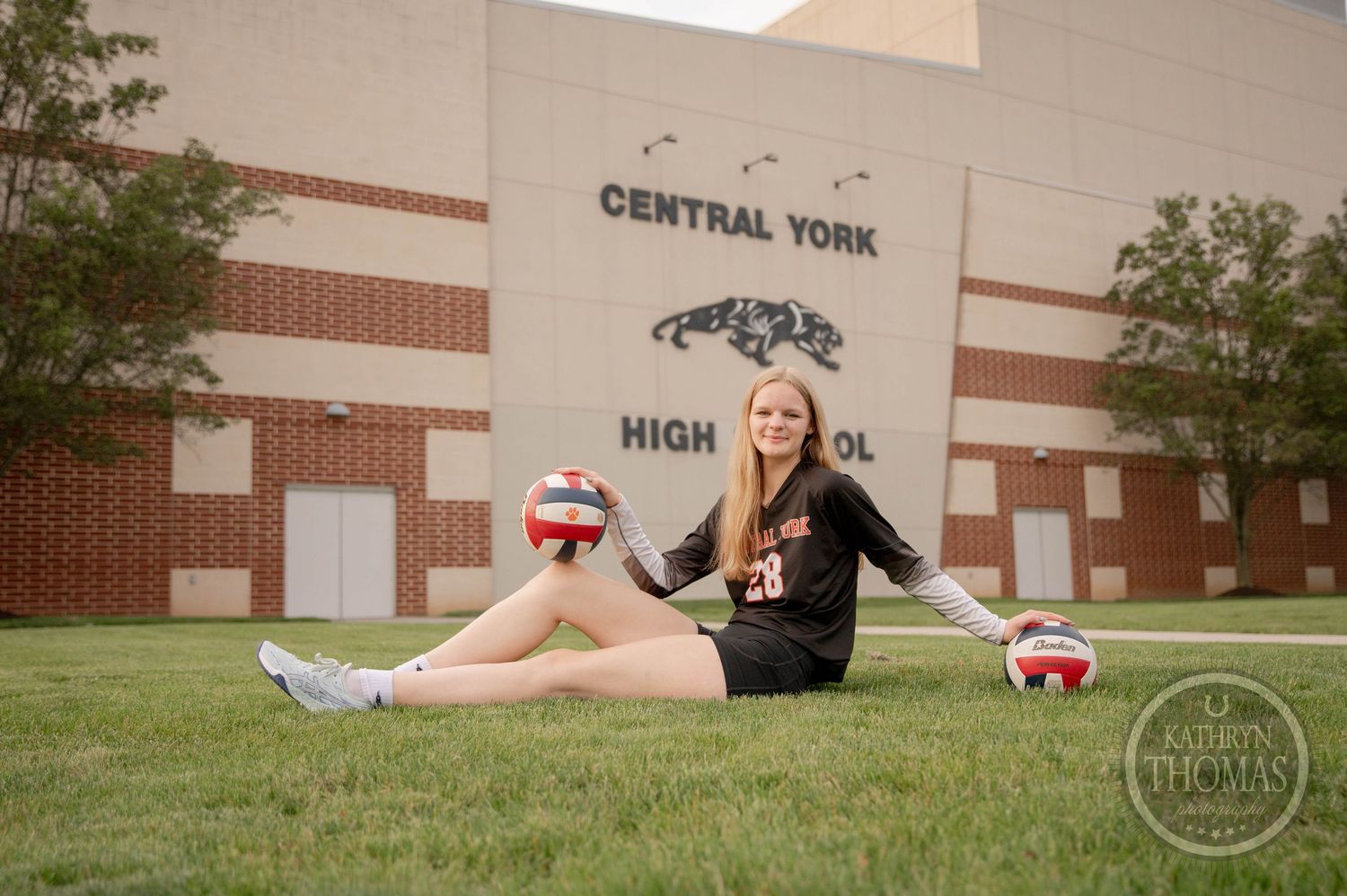 A cheerleader performs a split position while sitting on grass outside a brick building.
