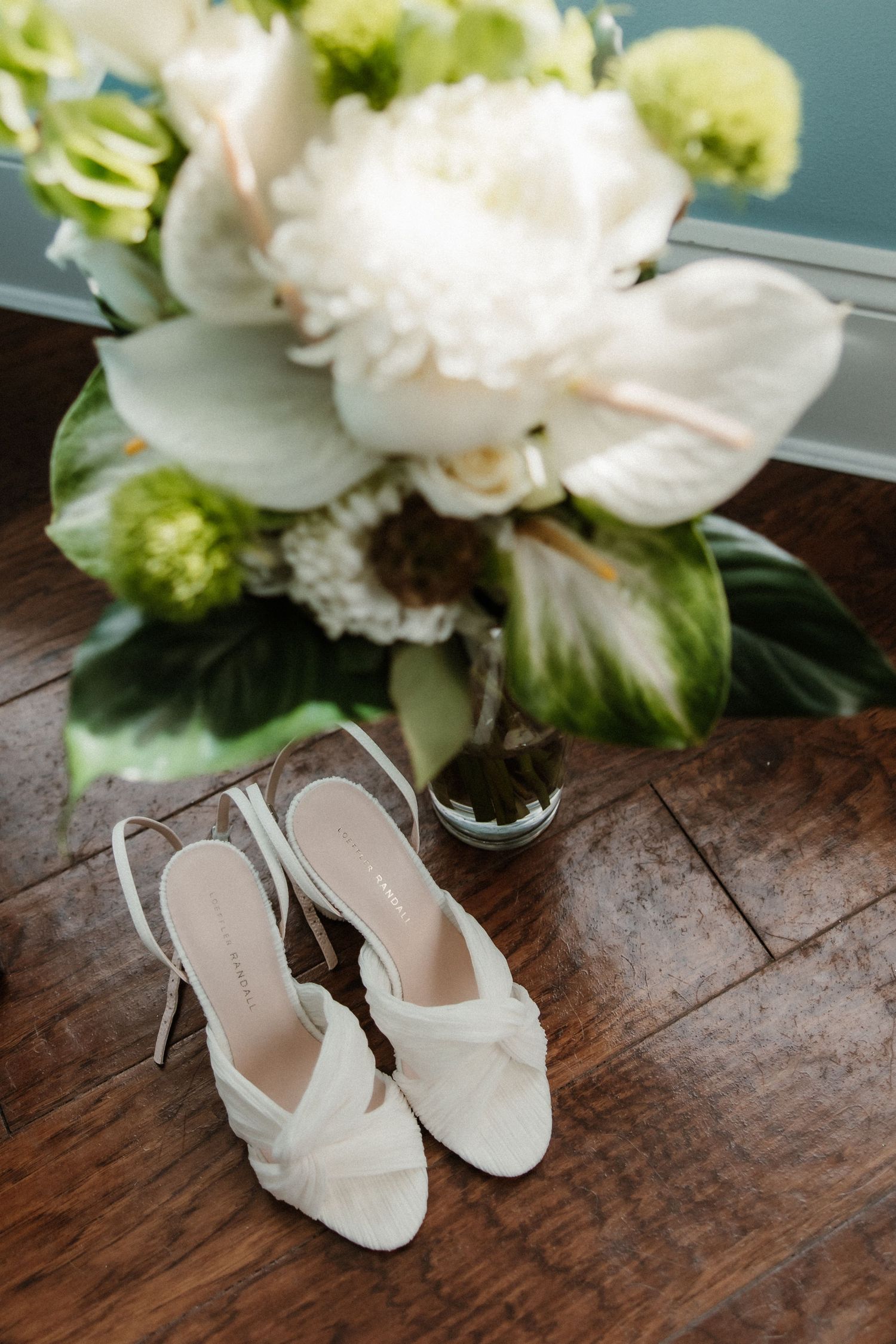 White wedding shoes and a delicate floral bouquet arrangement displayed on a rustic wooden surface.