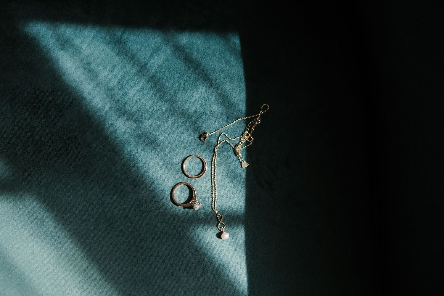 Wedding rings and a vintage key casting shadows on turquoise surface in dramatic lighting.