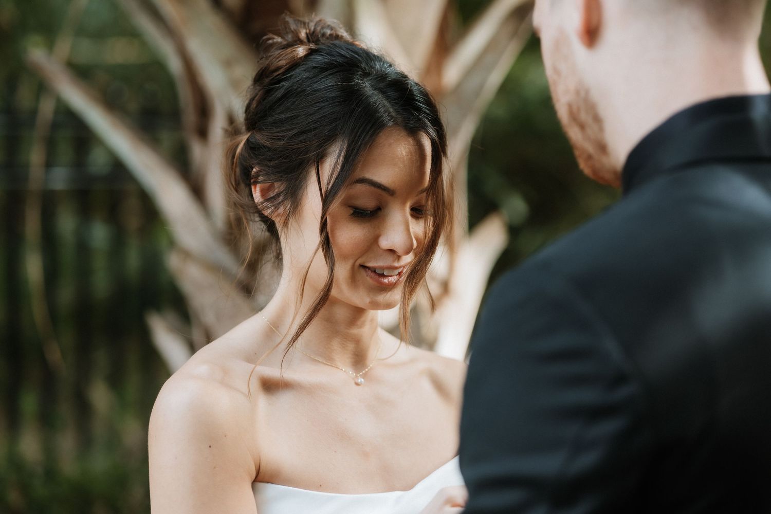 A couple sharing an intimate moment during their outdoor wedding ceremony with tropical plants in the background.