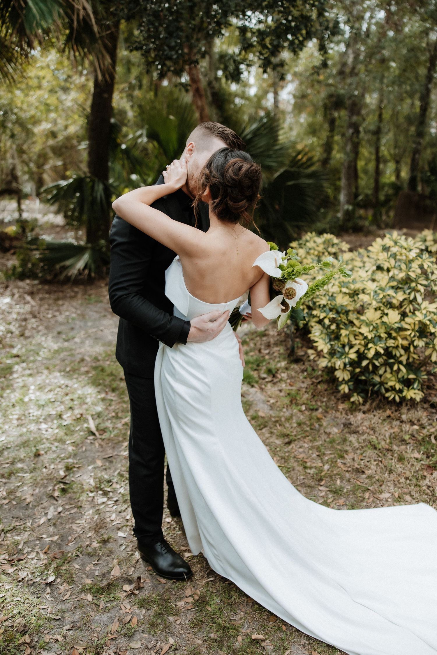 A romantic moment between newlyweds as the bride's white dress train flows in an outdoor garden setting.